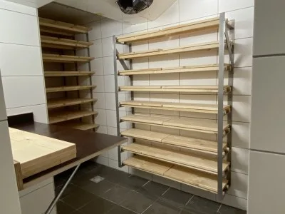 Holzregale an der Wand eines geflieseten Raums, daneben eine Arbeitsplatte aus Holz
