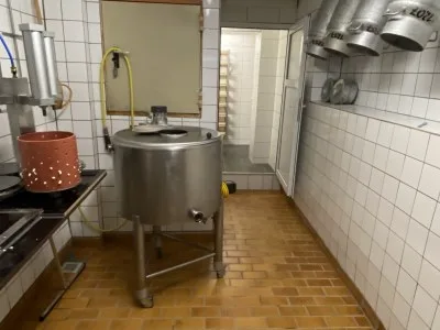 Edelstahlkessel auf Rollen in einem geflieseten Raum, rechts Abluftrohre an der Decke